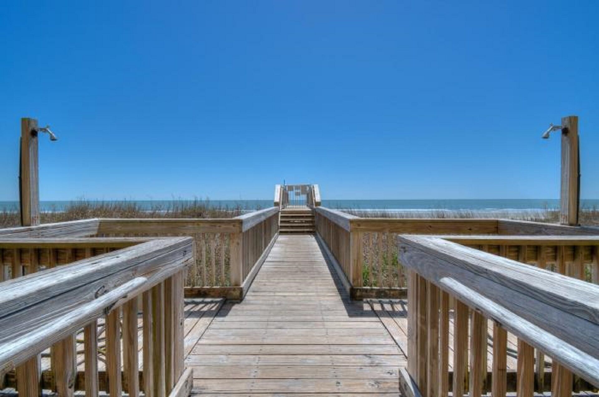 A wooden boardwalk leading to a beach with a clear blue sky.