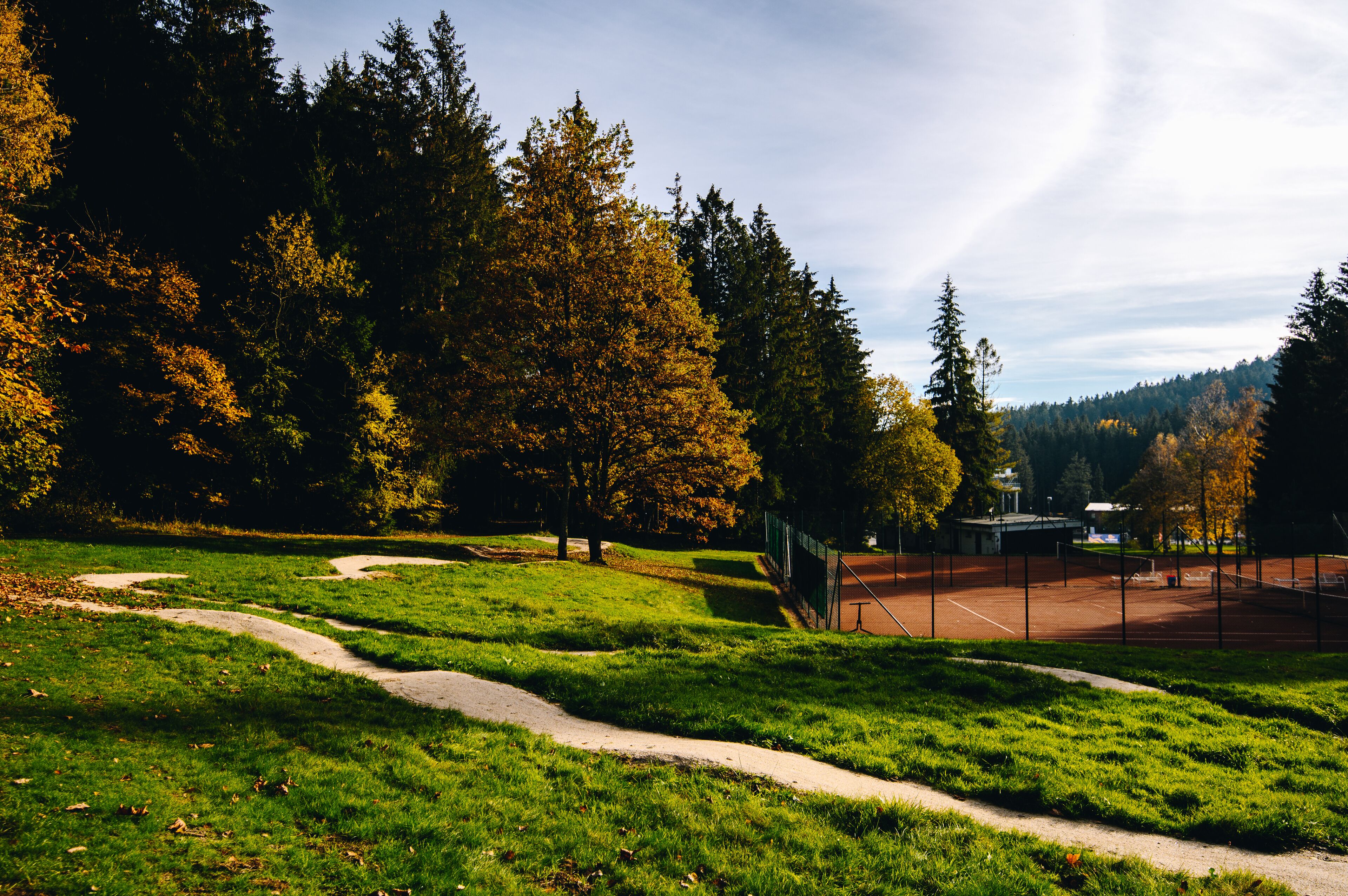 Un parque con cancha de tenis, un sendero sinuoso y árboles frondosos.