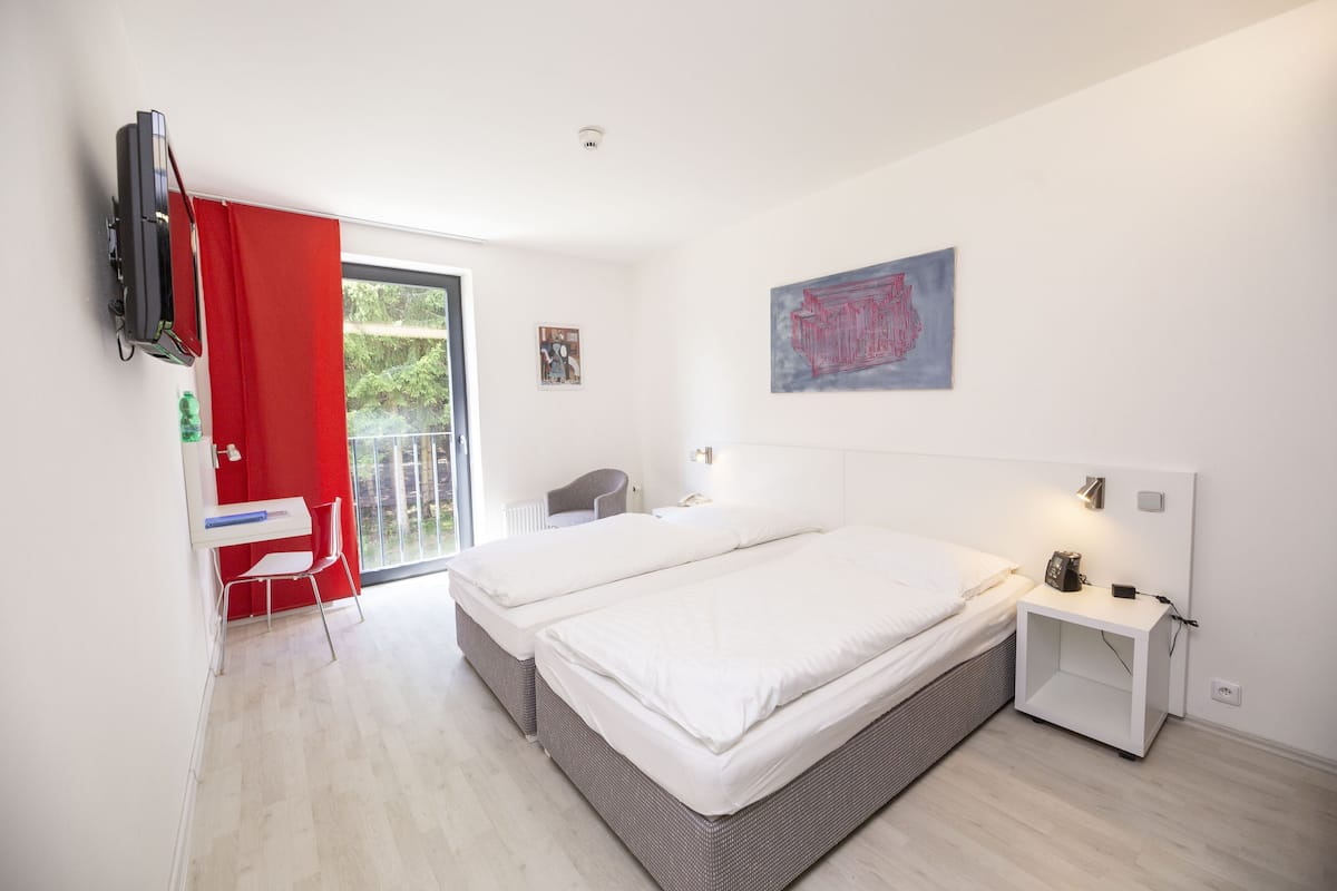 A bedroom with two beds, a desk, a chair, a TV, and artwork on the wall.