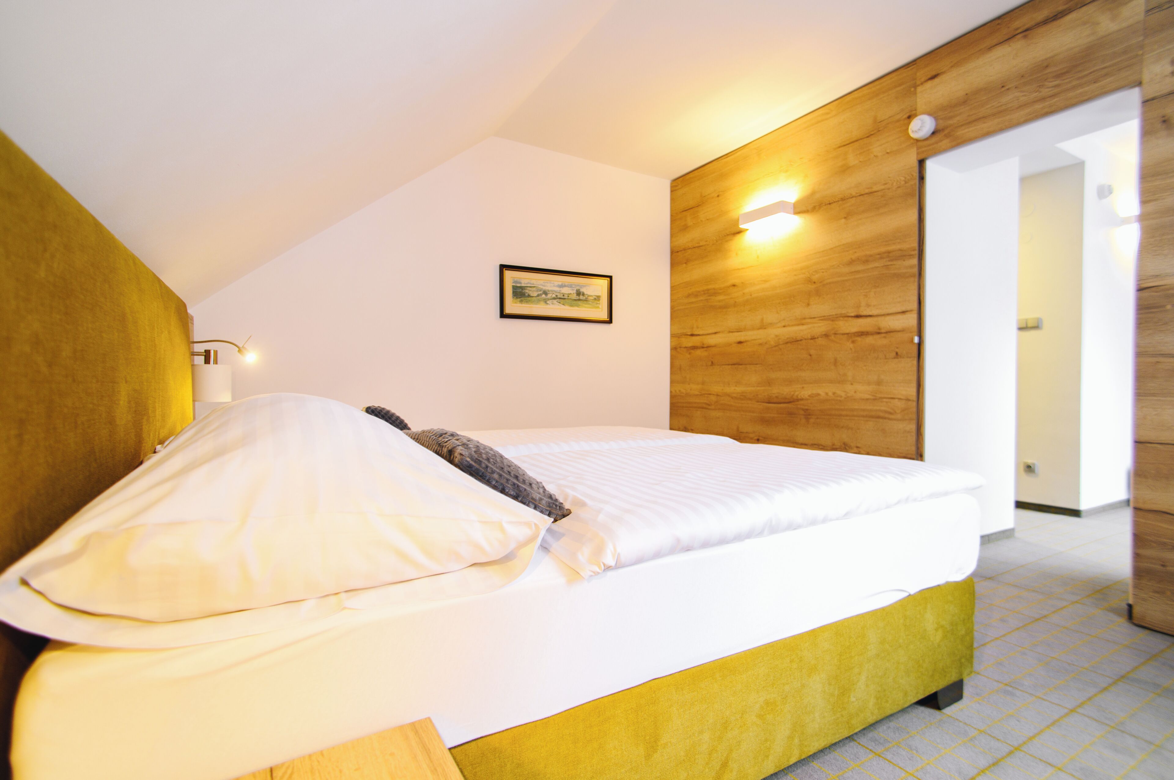 Una cama individual con cabecera de madera, una lámpara de noche y un cuadro en la pared.