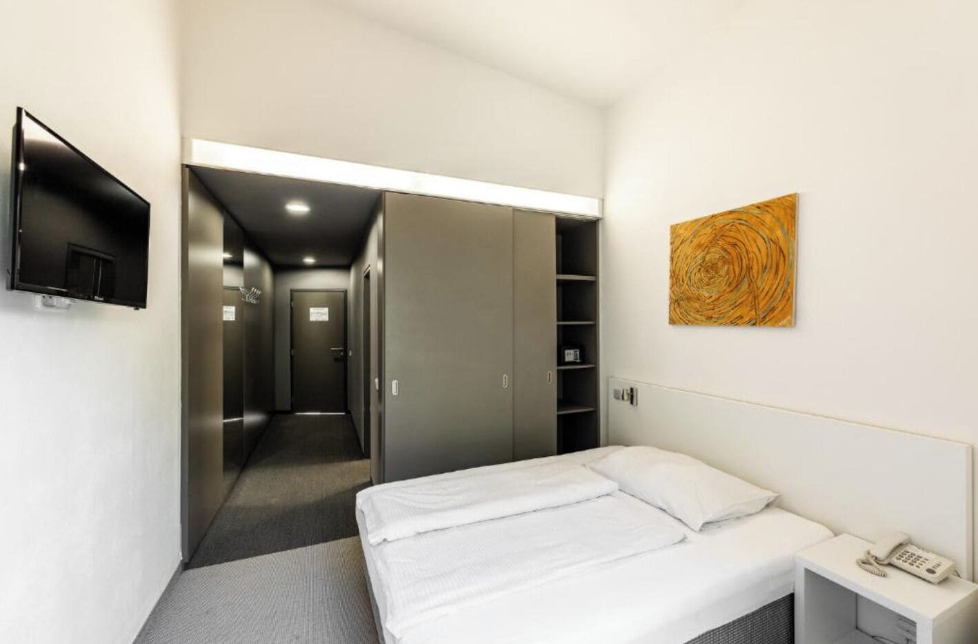 A hotel room with a bed, a TV, a wardrobe, and a painting on the wall.