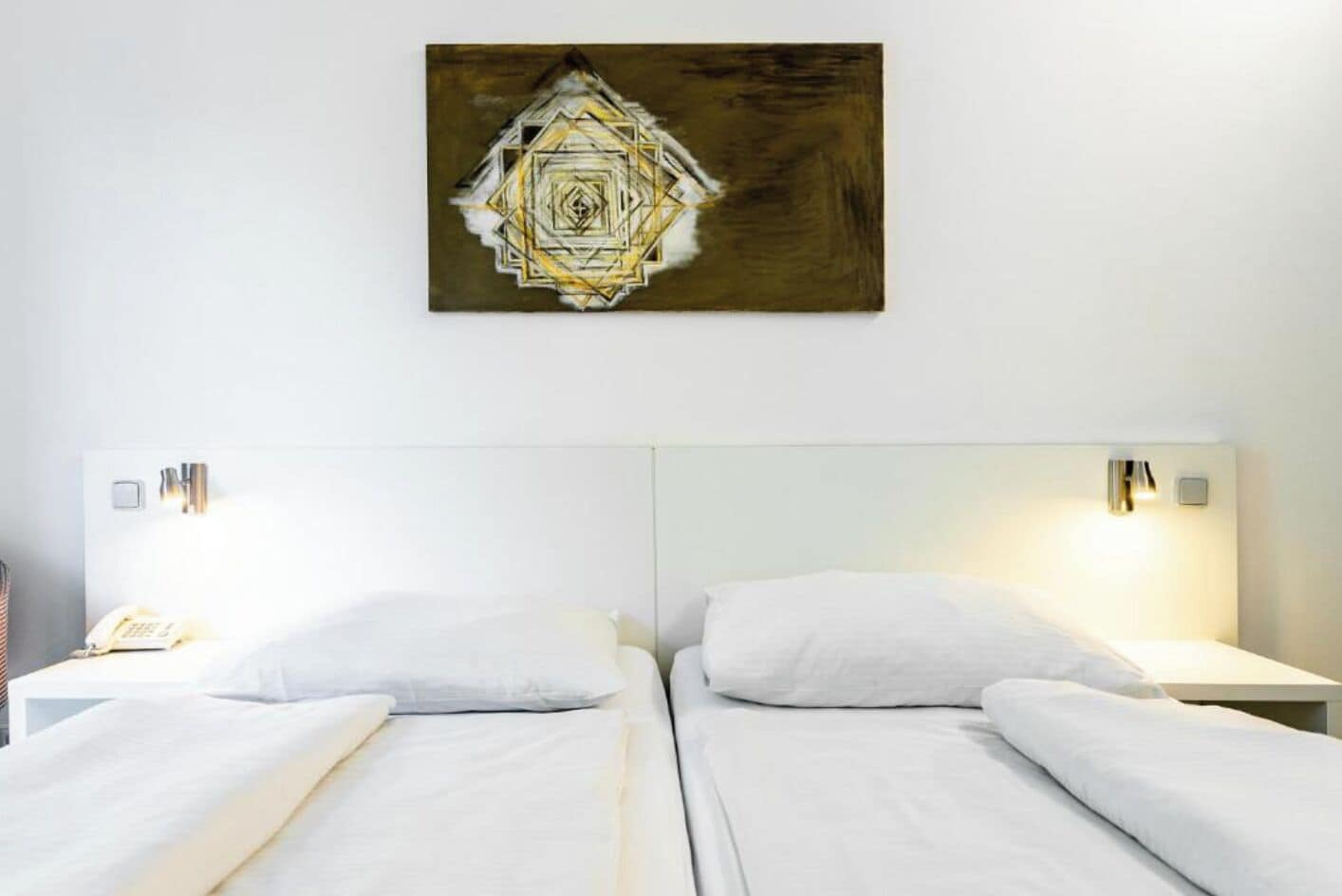 A hotel room with two beds, a wall-mounted artwork, bedside lamps, and a phone on the nightstand.