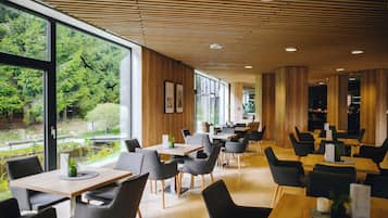 Un ristorante moderno con pannelli in legno a soffitto, ampie finestre con vista sul verde e diverse opzioni di posti a sedere.