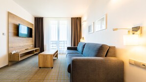 Una camera d'albergo moderna con divano, TV, tavolino in legno e vista sulla città attraverso ampie finestre.