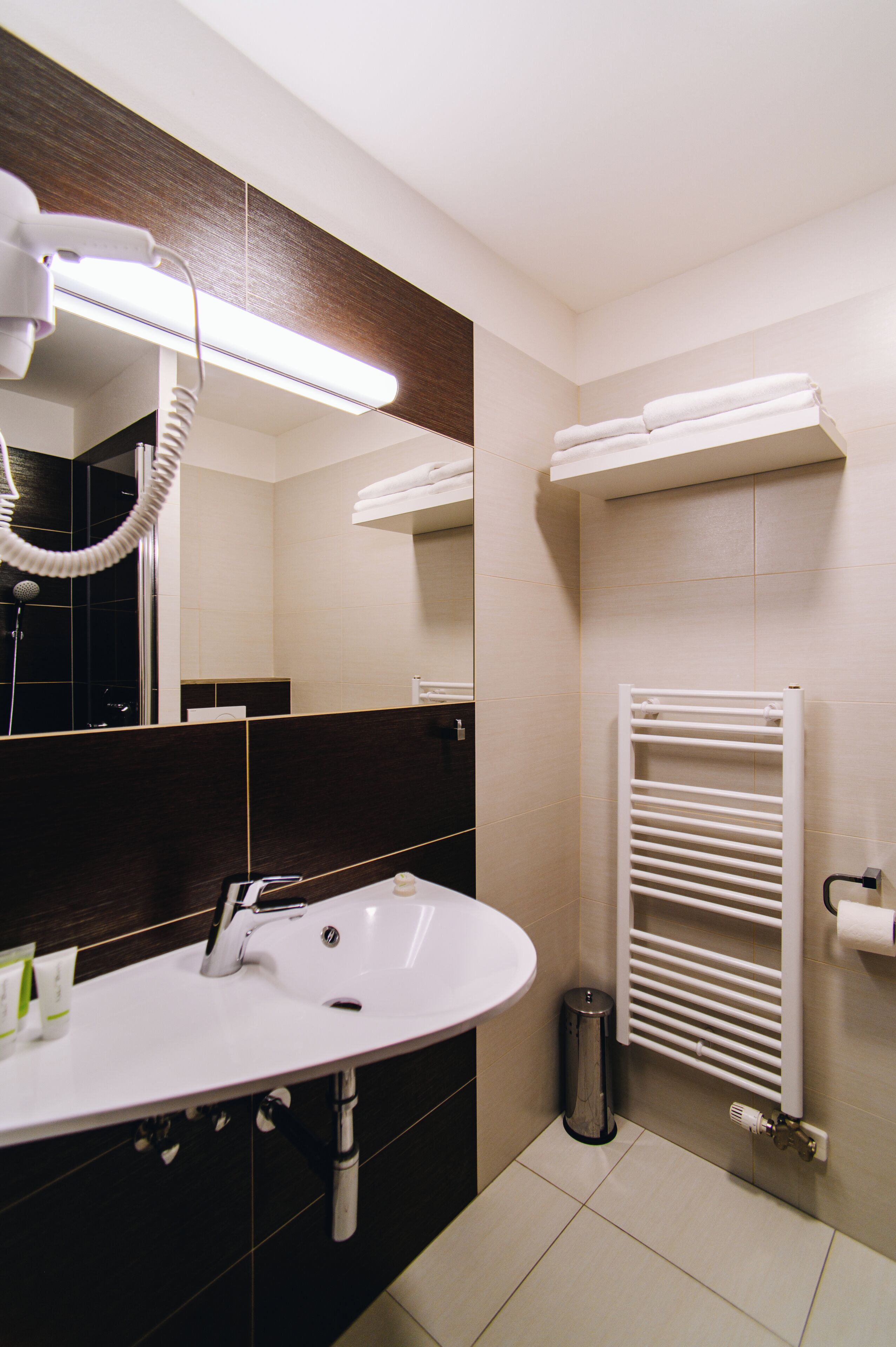 A bathroom with a white sink, a mirror, a hairdryer, a towel rack, and a radiator.