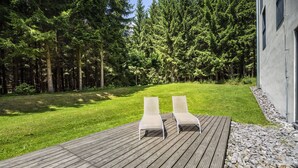 Un pontile di legno con due poltrone relax, immerso nel verde e circondato da alberi fitti.