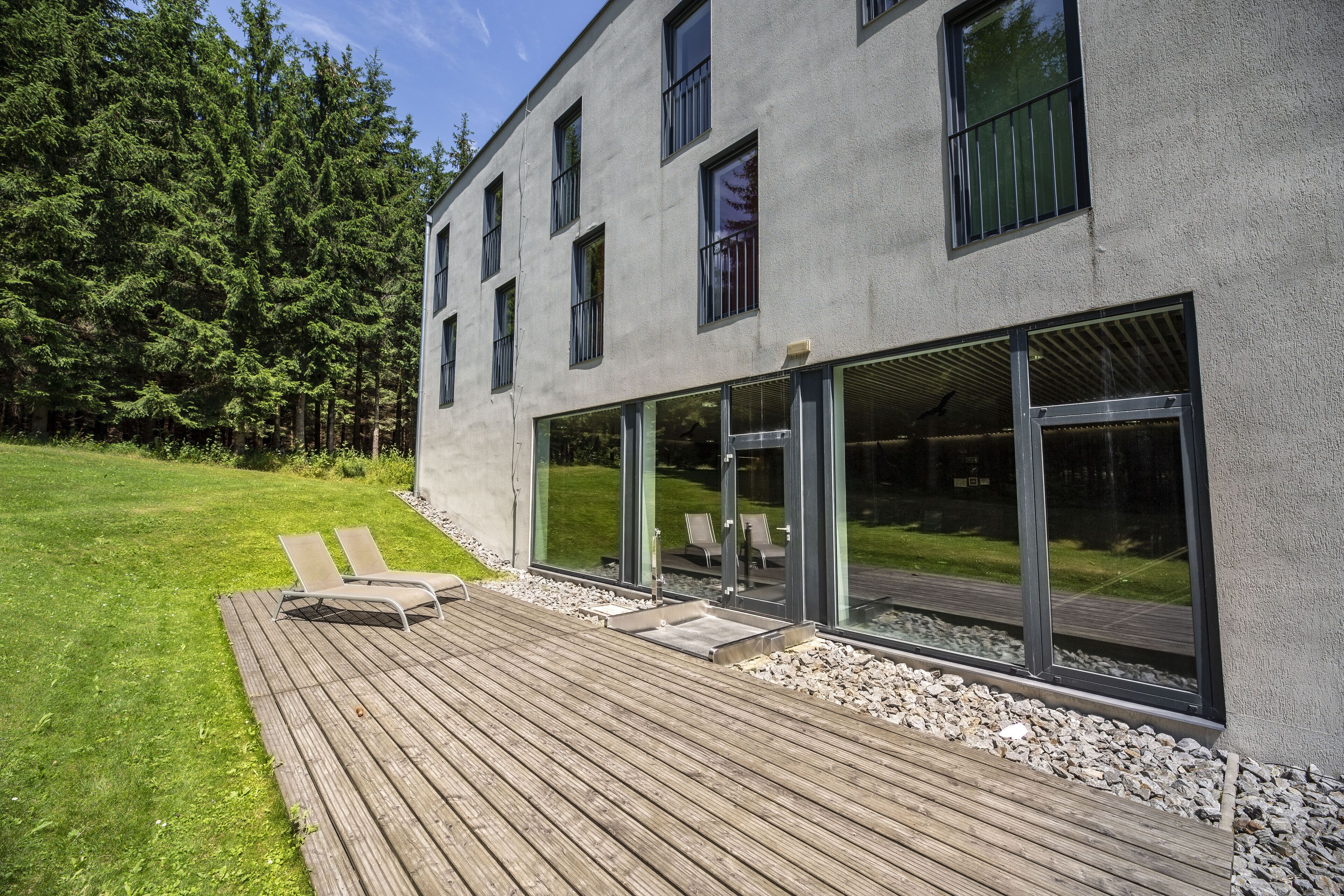 A modern building with a deck, large windows, and a grassy area.