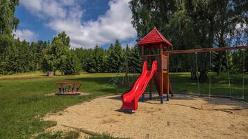 Une aire de jeux avec un toboggan rouge, une balançoire et une petite structure en bois.
