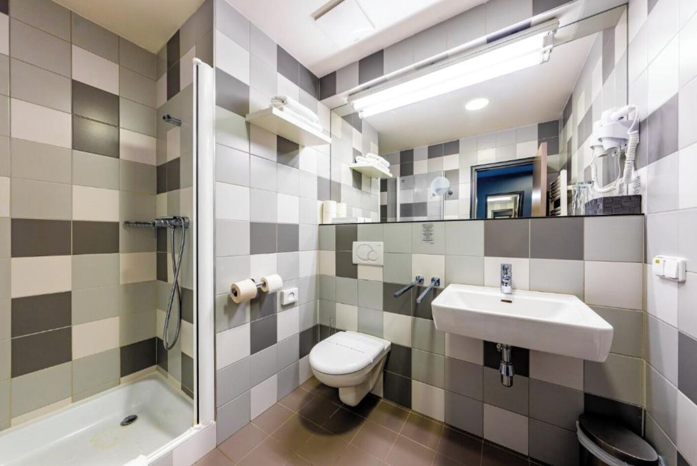 A modern bathroom with a shower, toilet, and sink, featuring checkered tile walls and a glass shower enclosure.