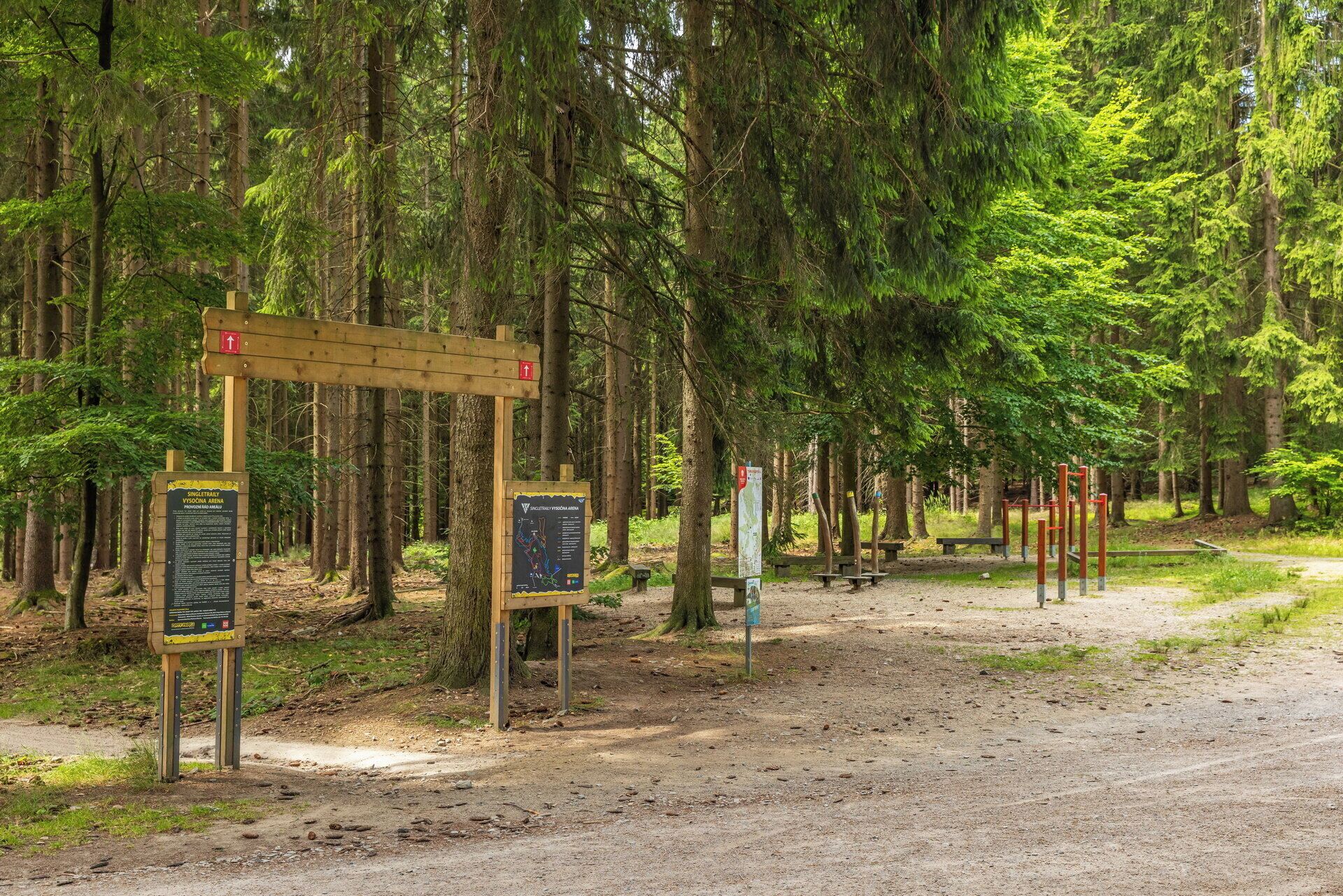 A forested area with a dirt path, wooden signposts, and picnic tables.
