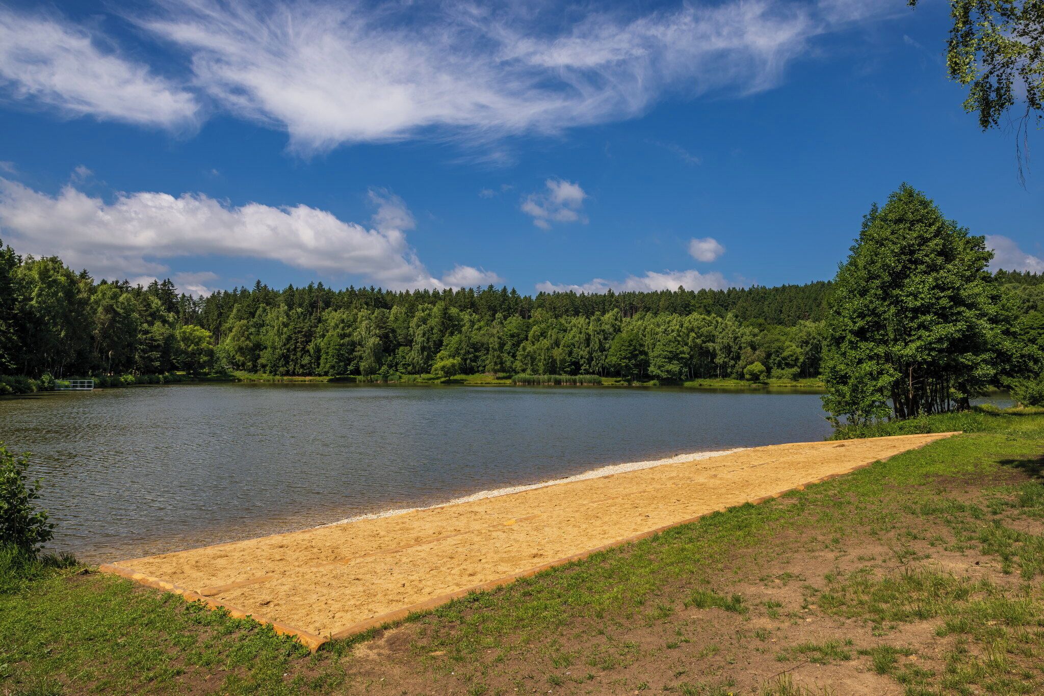 A lake with a sandy beach area, surrounded by dense forest.