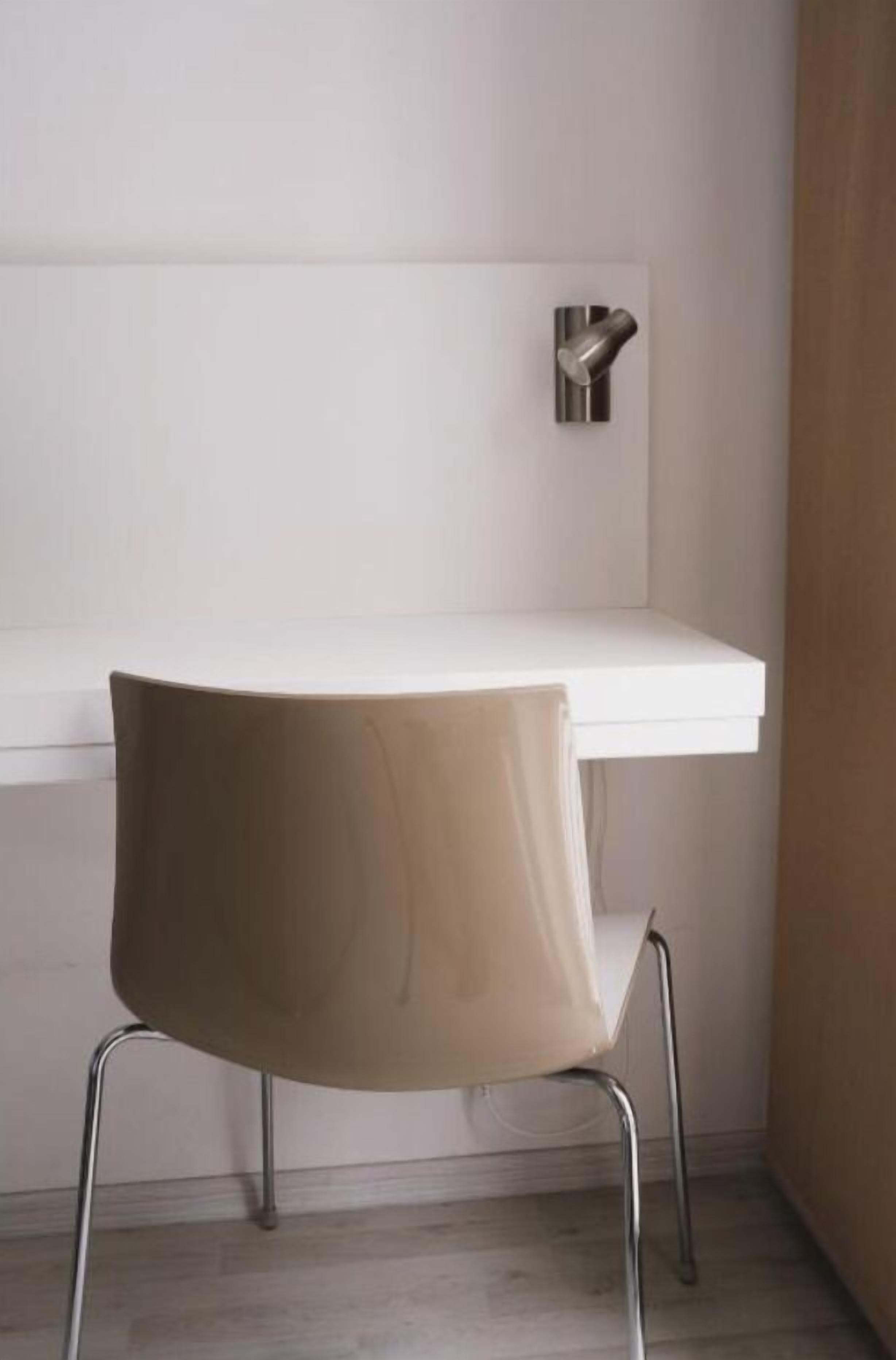 A corner of a room with a white wall, a white table, and a chair with metal legs.