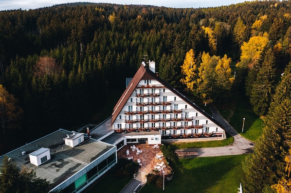 A large, multi-story hotel with a prominent triangular roof, surrounded by dense forest.