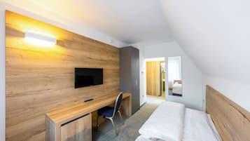 A modern hotel room with a wooden wall, a flat-screen TV, a desk with a chair, and a bed.