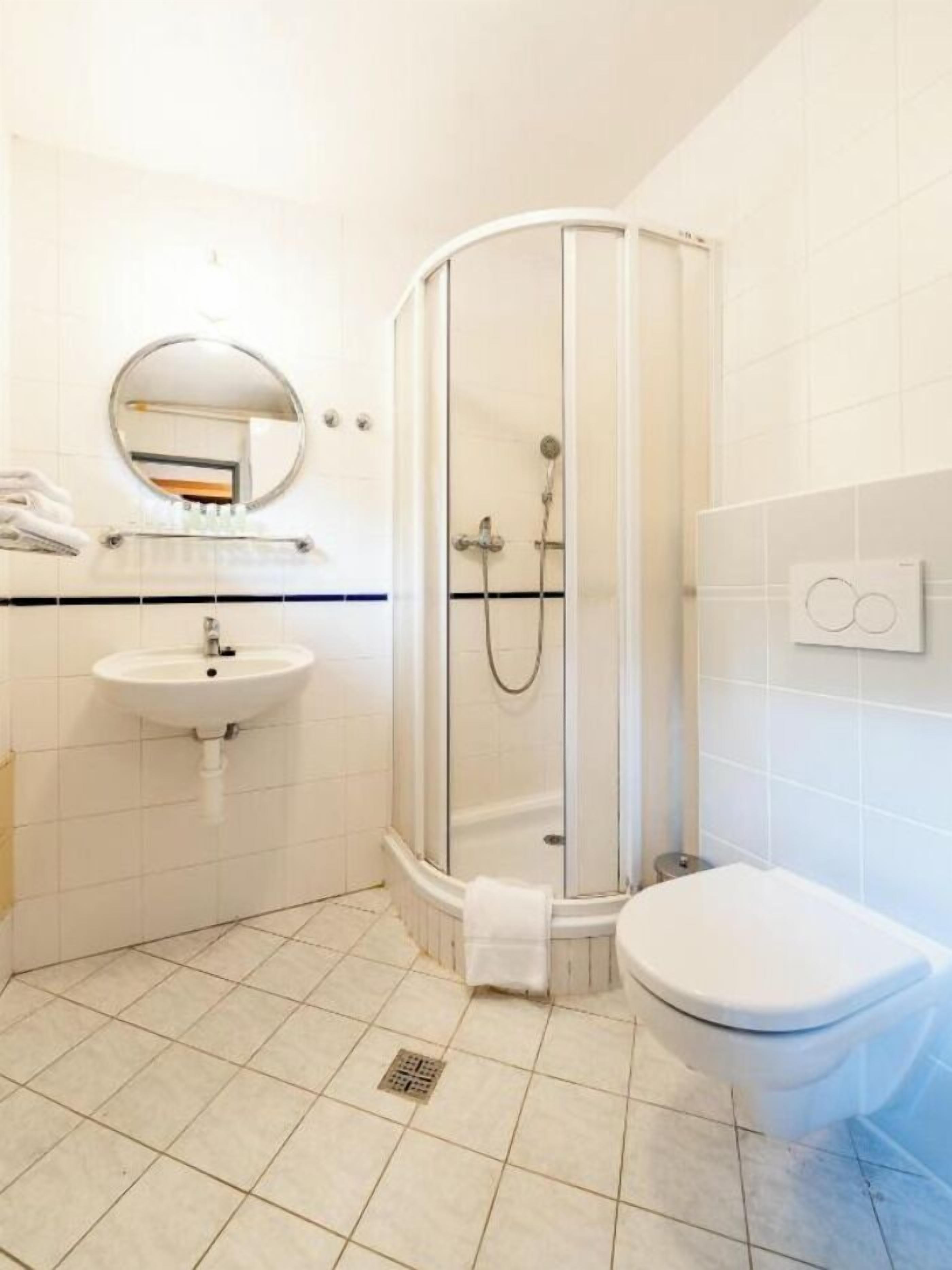 Een badkamer met douchecabine, wastafel, toilet en spiegel.
