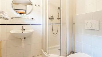 Een badkamer met douchecabine, wastafel, toilet en spiegel.