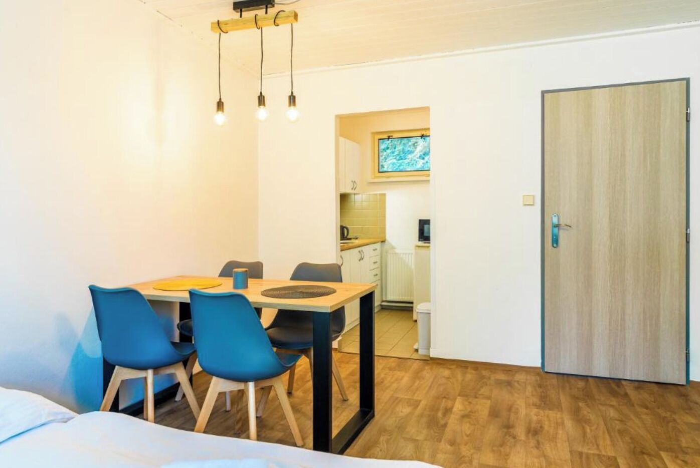 A compact room with a bed, a dining table with chairs, a kitchenette, and a door.