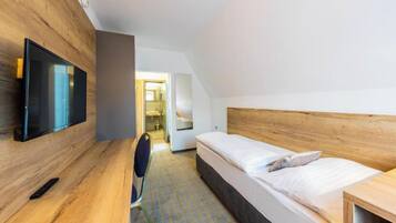 Une chambre d’hôtel moderne avec une tête de lit en bois, un téléviseur à écran plat fixé au mur, un lit avec du linge de lit blanc et un petit bureau avec une chaise.