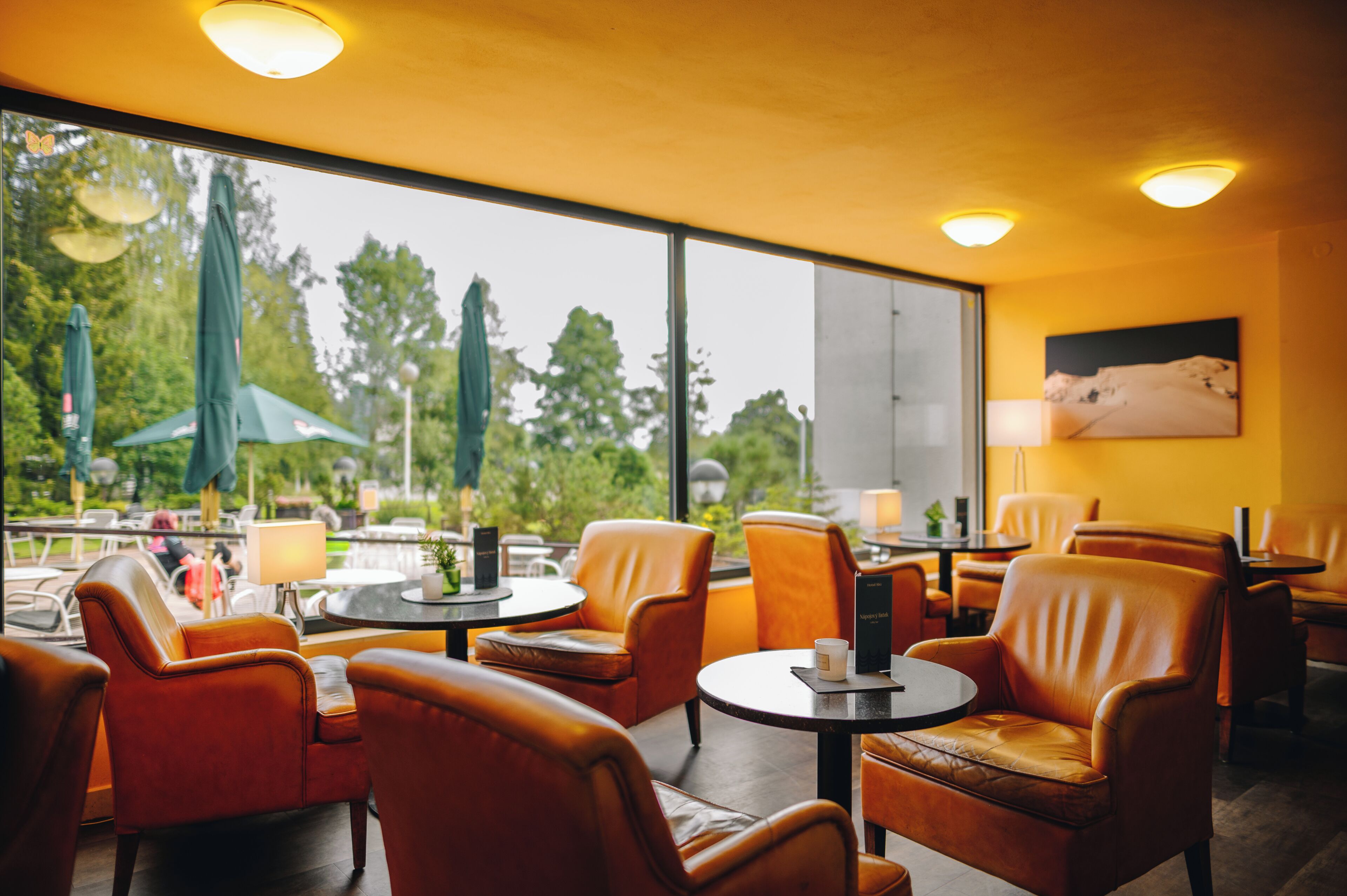 A restaurant with leather chairs, round tables, and a view of greenery outside.