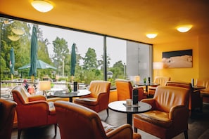 A restaurant with leather chairs, round tables, and a view of greenery outside. - Hotel Ski (Nové Mesto na Morave)
