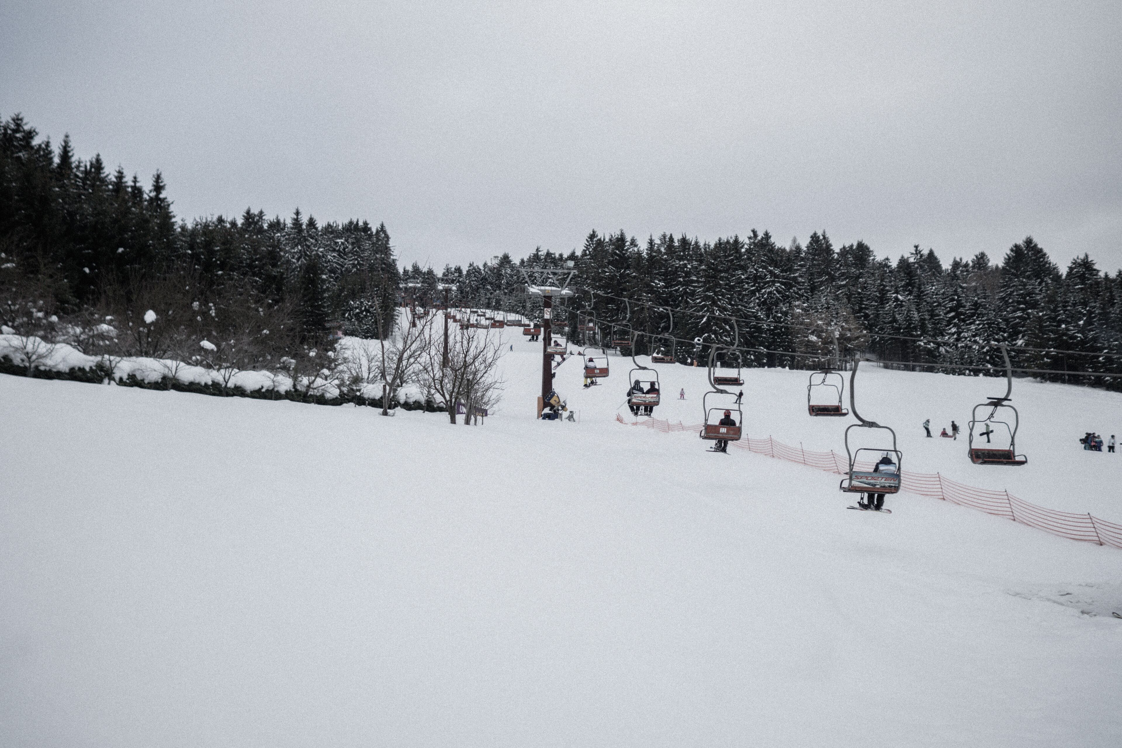 A ski lift with chairs moving up a snowy slope, surrounded by snow-covered trees.