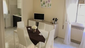 A dining area with a table set for four, a television on a stand, and a wall-mounted plant. - Lorenzo House Venice Mestre (Venezia)