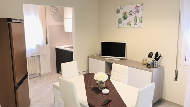 A modern kitchen with white appliances, a dining area with a brown table runner, and a TV on a wooden stand. - Lorenzo House Venice Mestre (Venezia)