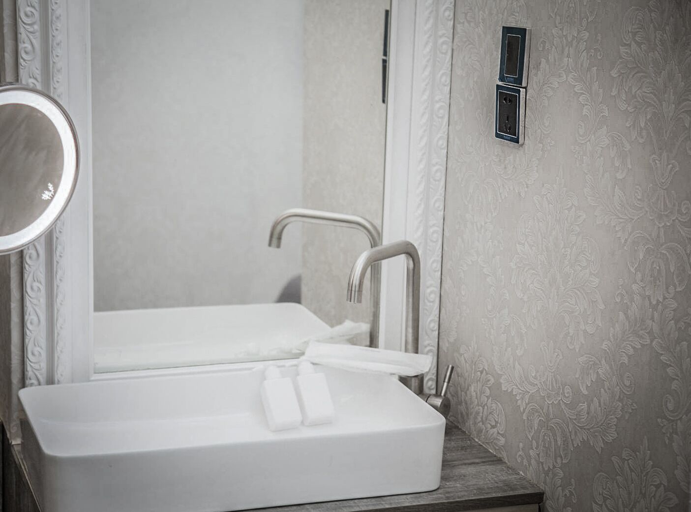 A bathroom with a white sink, a mirror, and a wall-mounted light fixture.