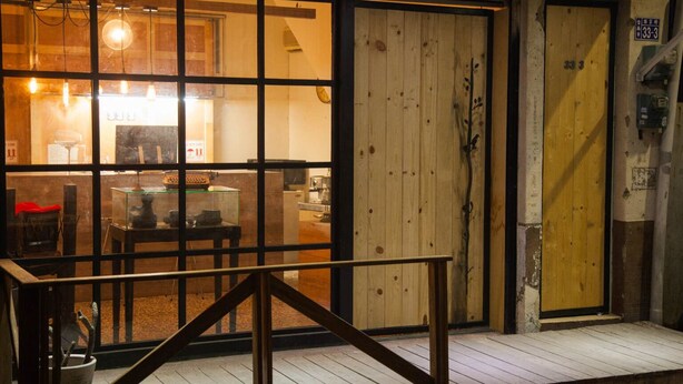A wooden door with a number sign, a glass display case with items inside, and a wooden staircase leading to a porch. - Summer night (Tainan)