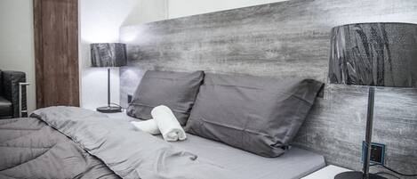 Una cama bien hecha con ropa de cama gris, cabecera de madera y dos lámparas de noche.