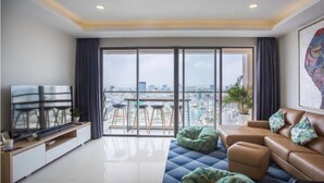 A modern living room with a large TV, comfortable seating, a balcony with a city view, and a dining area. - Millennium Masteri Apartment (Ho Chi Minh City)