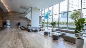 A spacious lobby with a modern design, featuring a staircase, seating area, and large windows offering views of the city. - Millennium Masteri Apartment (Ho Chi Minh City)