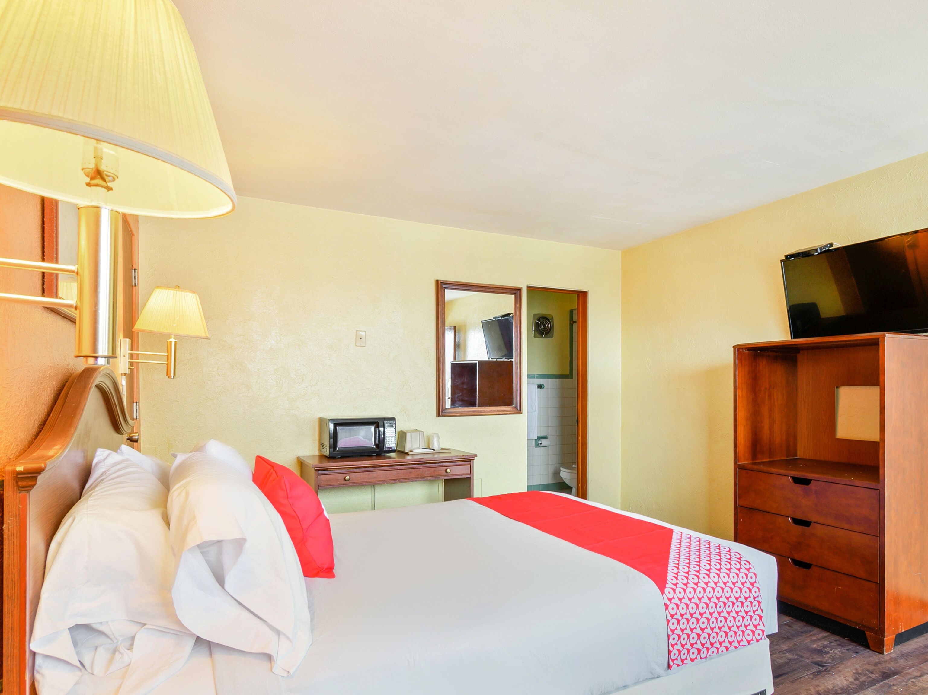 A hotel room with a bed, a television, a desk with a microwave, and a wardrobe.