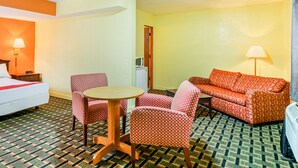 A hotel room with a bed, a sofa, a dining table with chairs, a microwave, and a lamp. - OYO Hotel Downtown Peoria I-74 (Peoria)