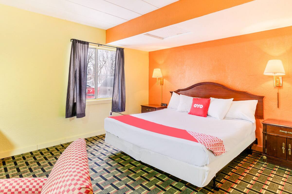 Una habitación de hotel con una cama grande, dos mesitas de noche, un ventanal con cortinas y un suelo estampado.
