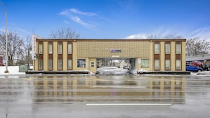A motel with a central entrance, a parking lot, and a clear sky. - OYO Hotel Downtown Peoria I-74 (Peoria)