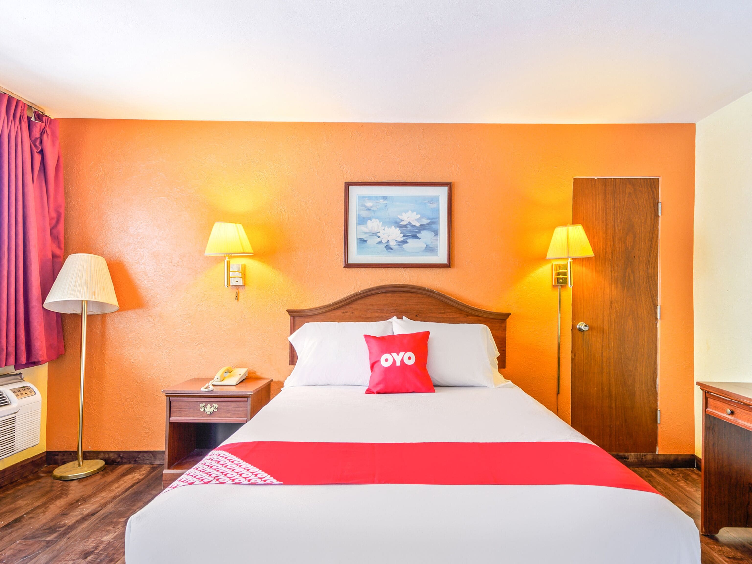 A hotel room with a large bed, two bedside lamps, a wooden nightstand with a telephone, and a door.