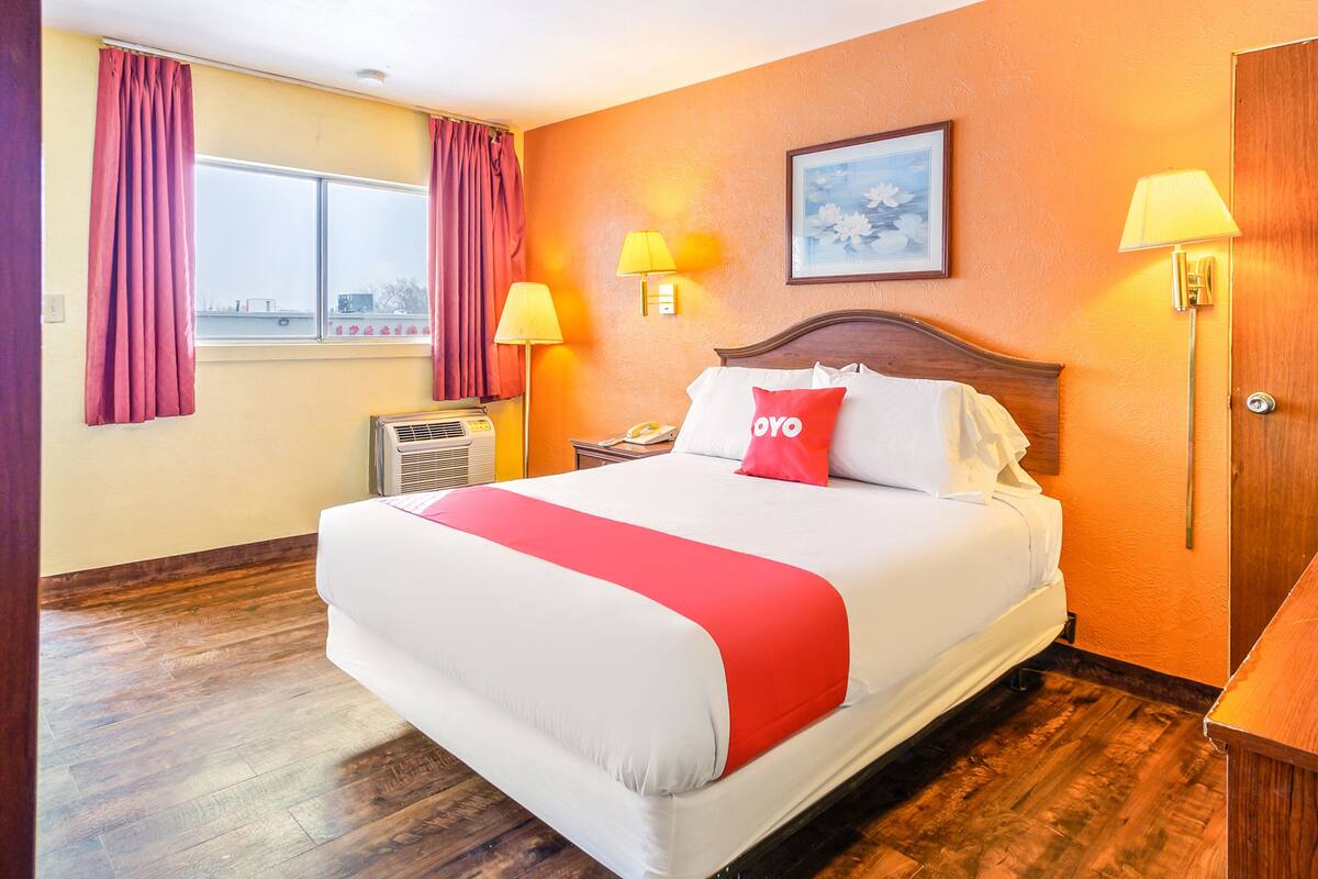 Habitación de hotel con una cama grande, dos lámparas de noche, una ventana con cortinas e imagen enmarcada en la pared.