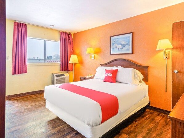 A hotel room with a large bed, two bedside lamps, a window with curtains, and a framed picture on the wall. - OYO Hotel Downtown Peoria I-74 (Peoria)