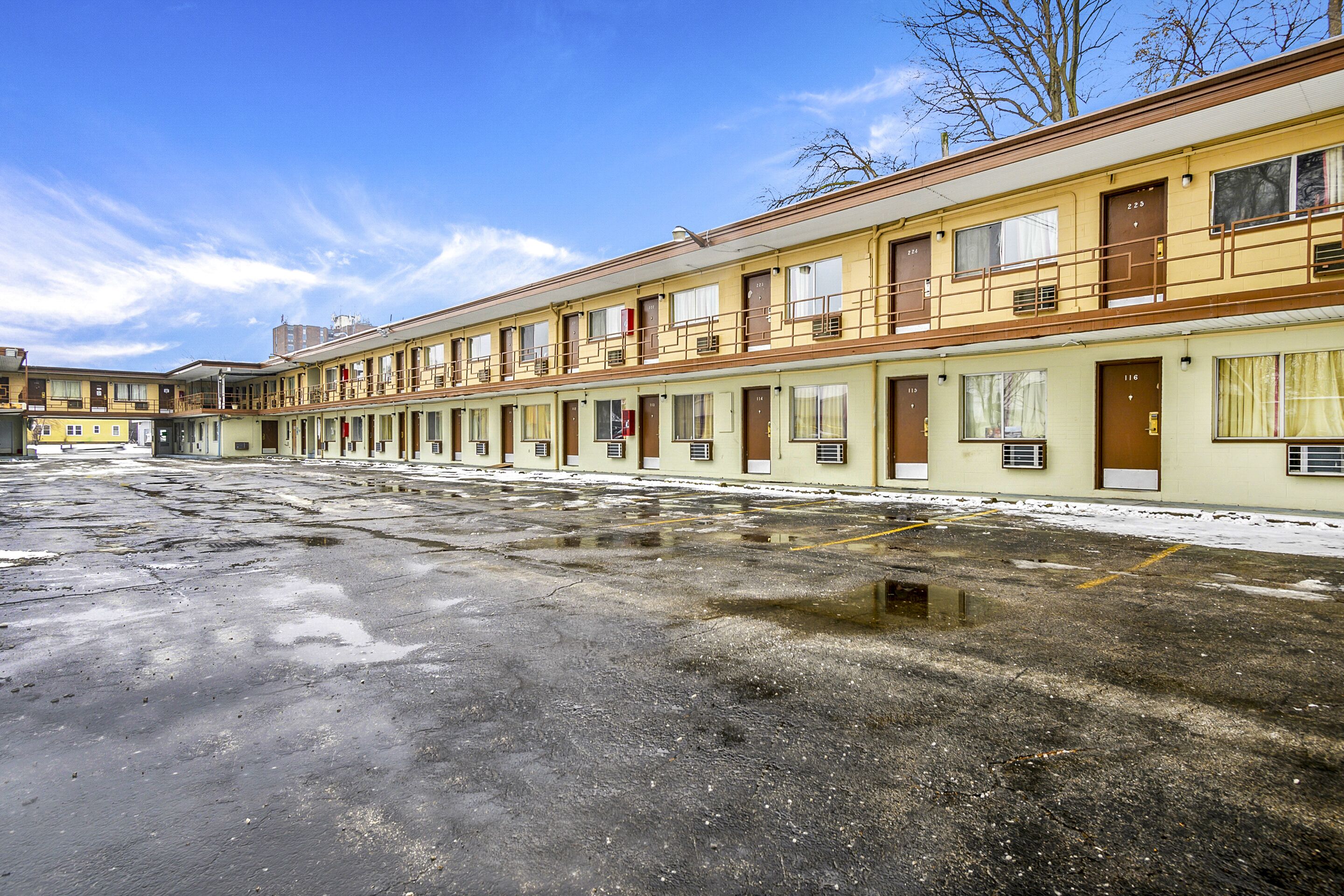 A row of motel rooms with a parking lot in front.