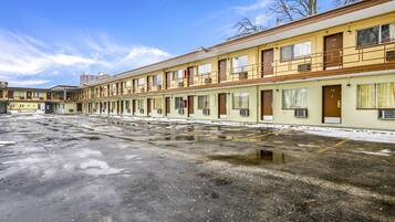A row of motel rooms with a parking lot in front.