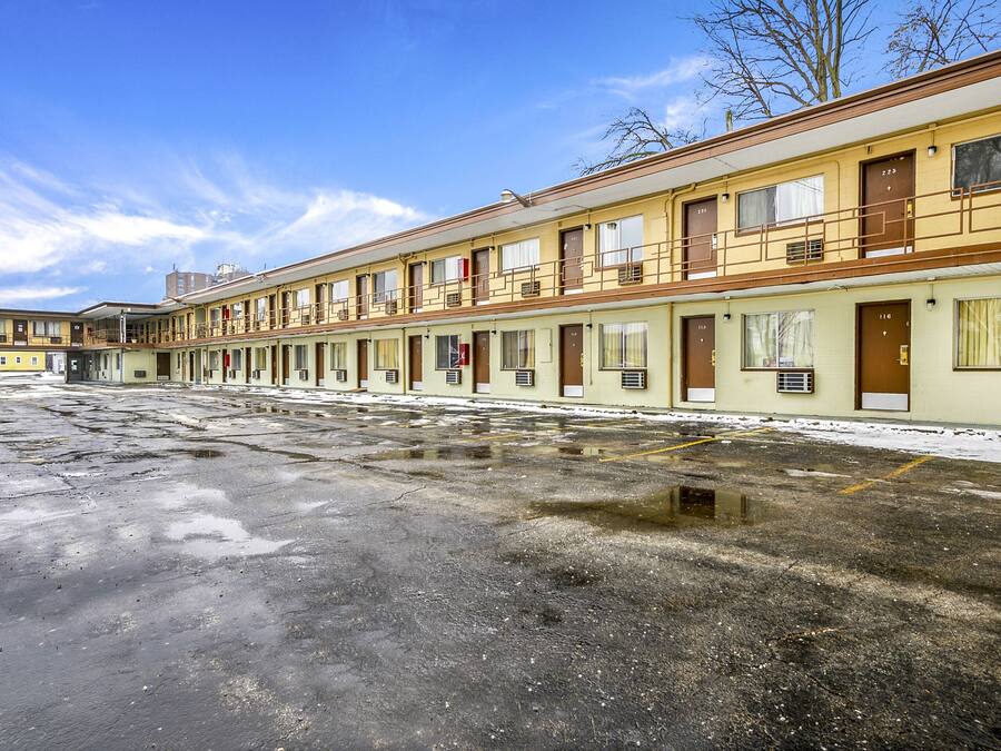 A row of motel rooms with a parking lot in front.