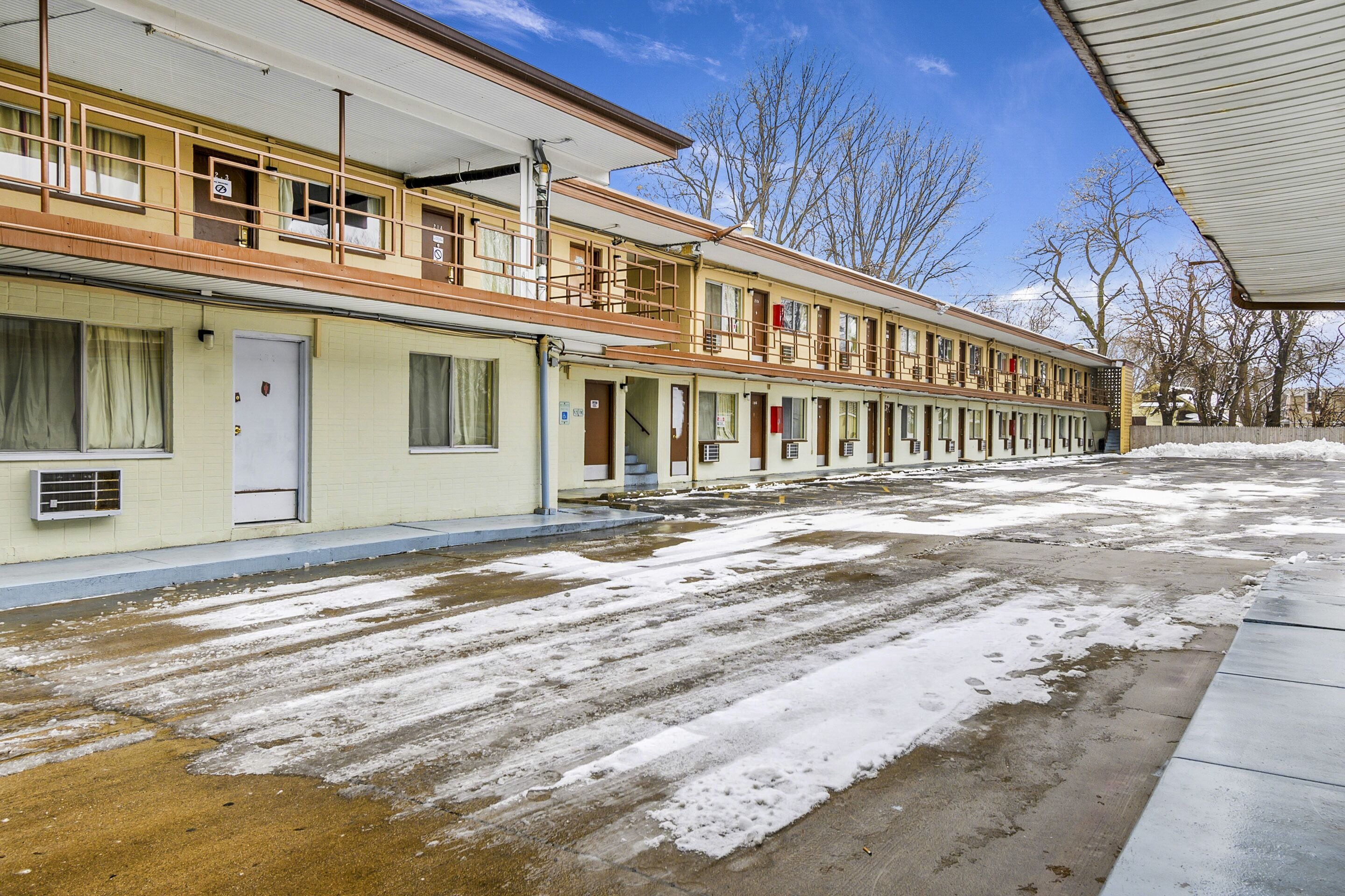 A row of motel rooms with a covered walkway and a snow-covered ground.