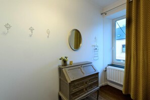 Une petite pièce comprenant une commode, un miroir et une fenêtre donnant sur un immeuble.