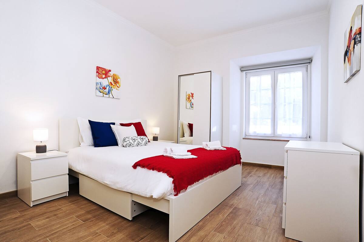 Un dormitorio moderno con cama, mesitas de noche, cómoda y ventana.