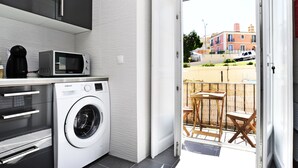 A compact kitchen with a washing machine, microwave, and coffee maker. - Oeiras  Apartment (Oeiras)