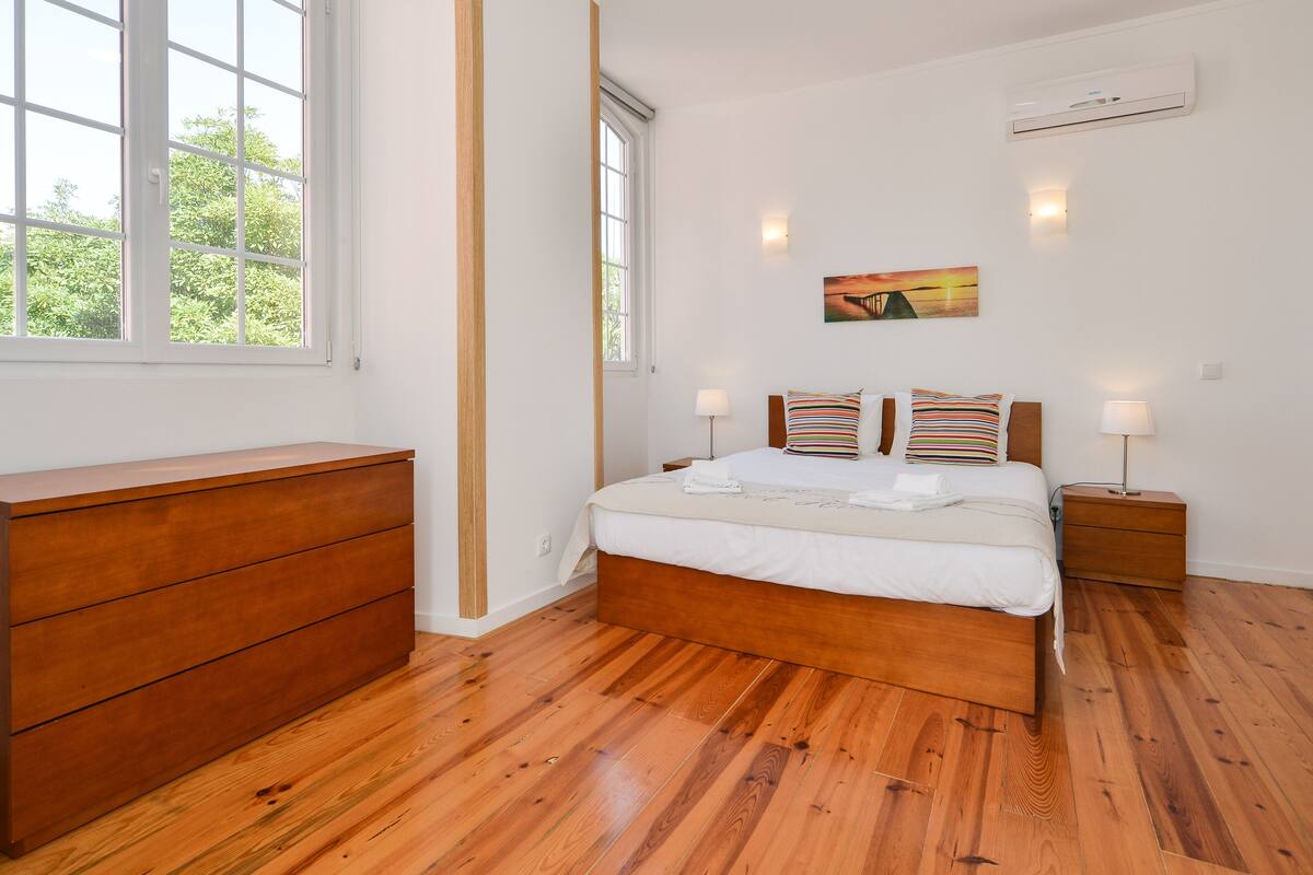 Un dormitorio con una cama y un aparador de madera, una ventana y un equipo de aire acondicionado.