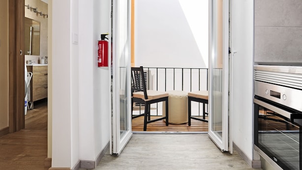 A modern apartment with a wooden floor, a balcony with a chair and a small table, a fire extinguisher, and a kitchen area with an oven. - Oeiras  Apartment (Oeiras)