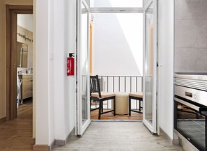 A modern apartment with a wooden floor, a balcony with a chair and a small table, a fire extinguisher, and a kitchen area with an oven. - Oeiras Apartment (Oeiras)