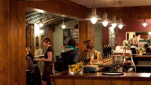 Un espace bar avec des meubles en bois, un barman et un comptoir où sont exposées des bouteilles et des verres.